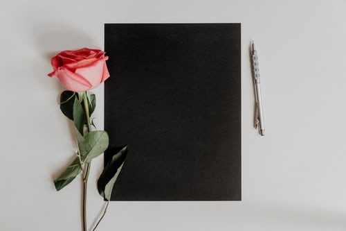 A black notebook, decorative pen, and pink rose flat lay photo