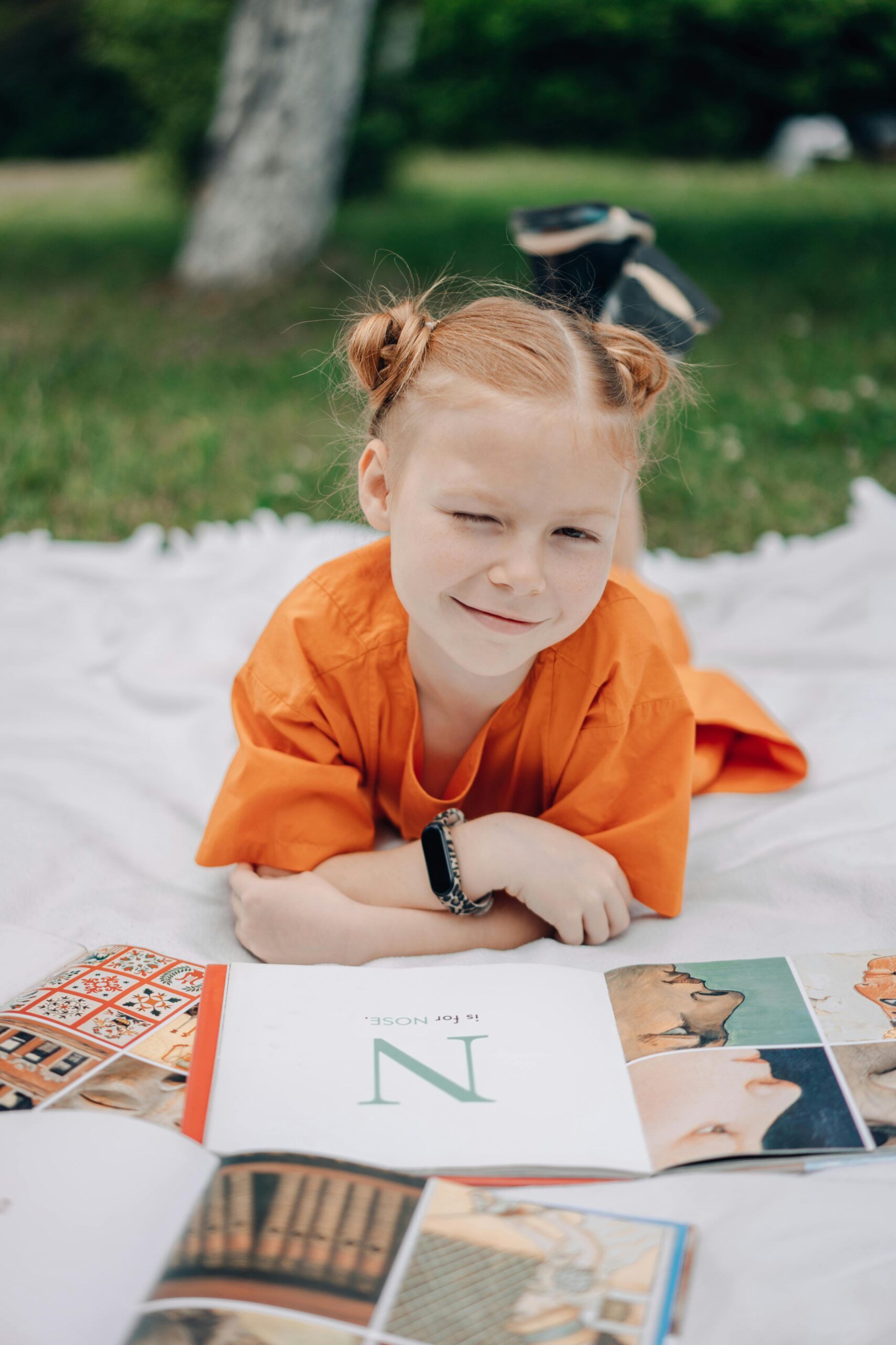 Little girl sitting on a blanket outside with school books