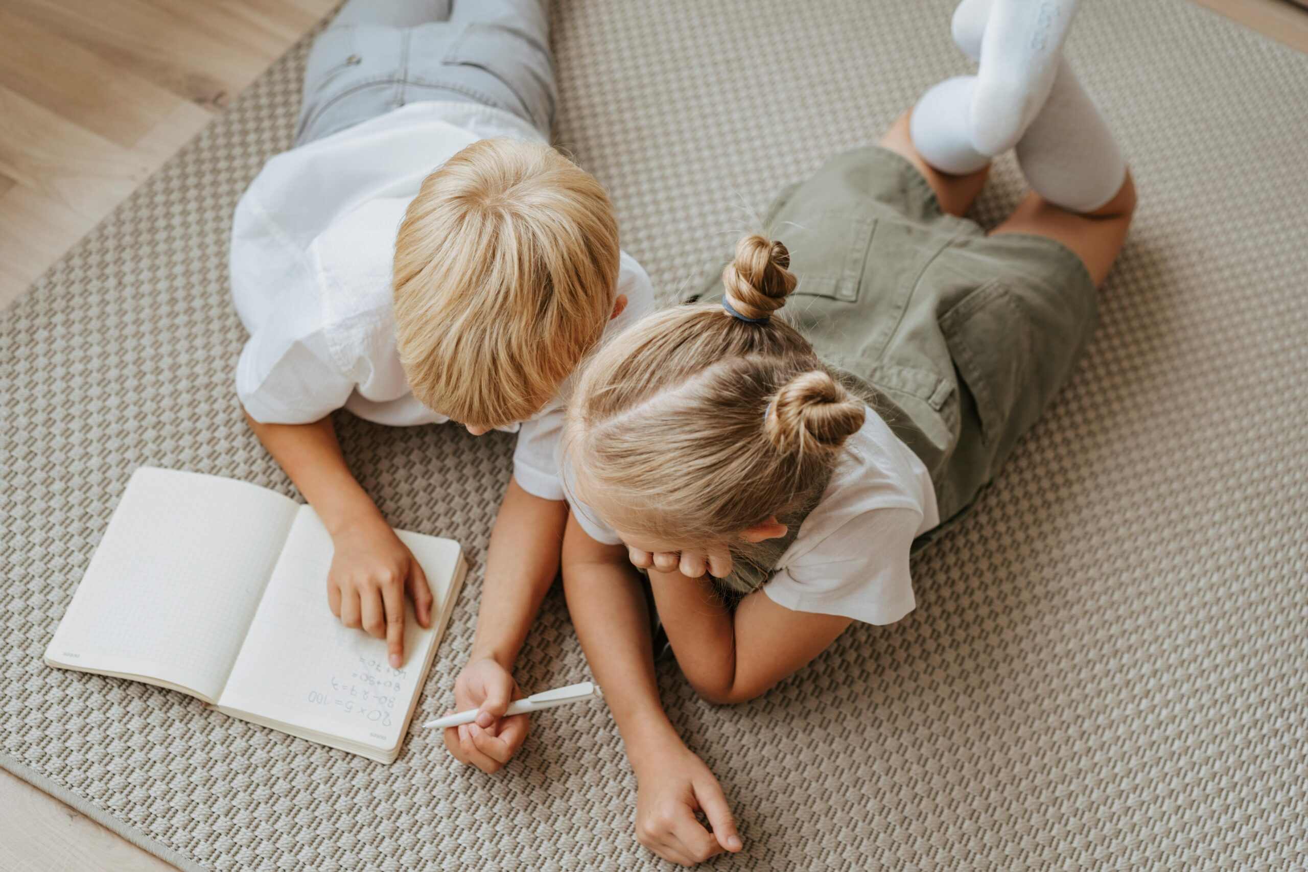 A little boy and girl sitting on the floor with a book possibly working on a homeschool project